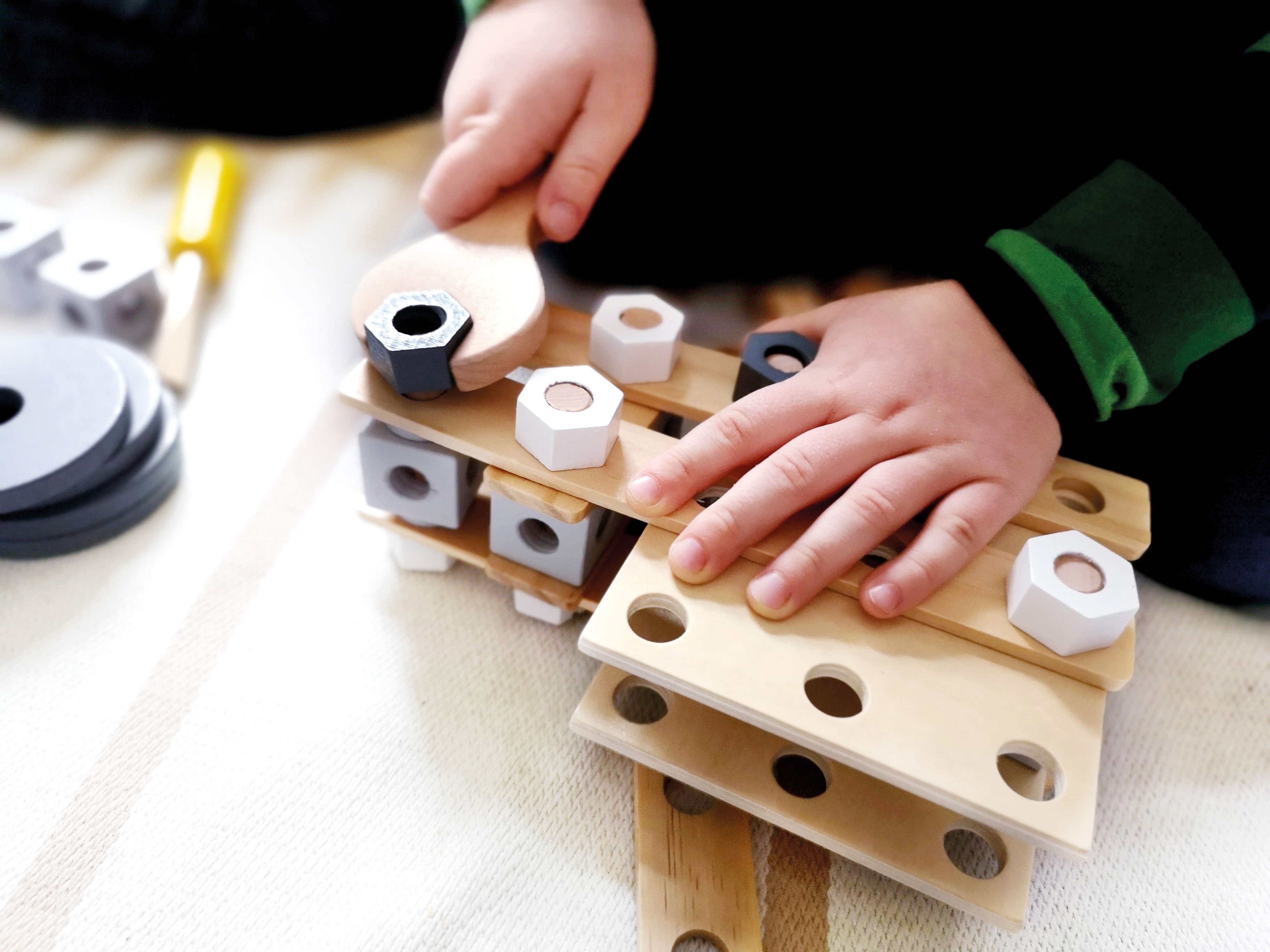 Kinderhände drehen mit Schraubenschlüssel Holzschraube in Spielzeug