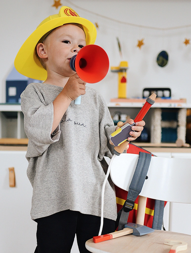 Junge mit Spielzeug-Megafon und Feuerwehrspielzeug aus Holz