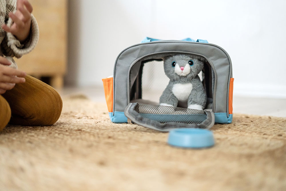Kind spielt mit Plüschkatze, Tasche und Pflegeset