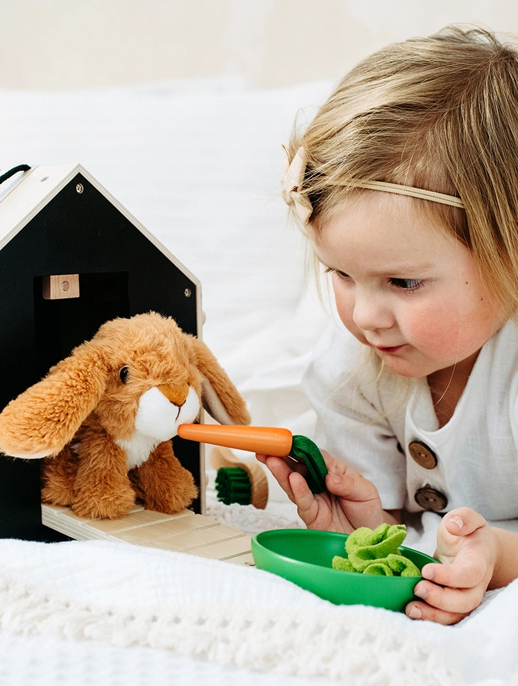 Mädchen spielt mit Plüsch-Hase und Hasenstall aus Holz