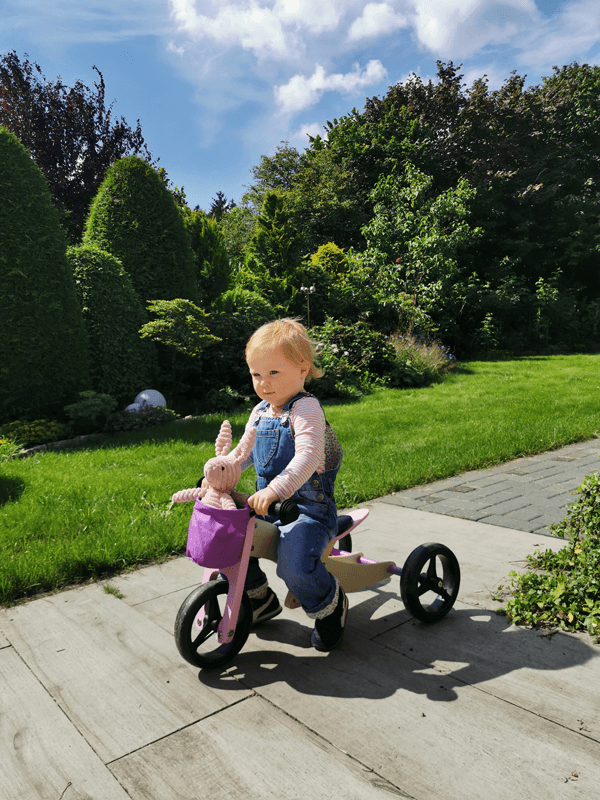 Mädchen im Garten auf rosa Dreirad