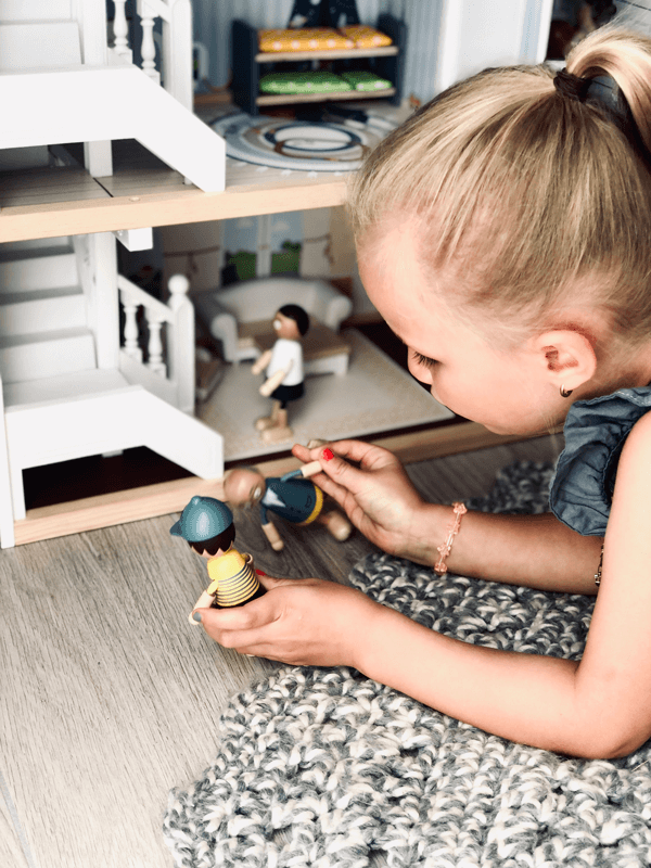 Kind spielt mit Puppenhaus aus Holz und Spielfiguren