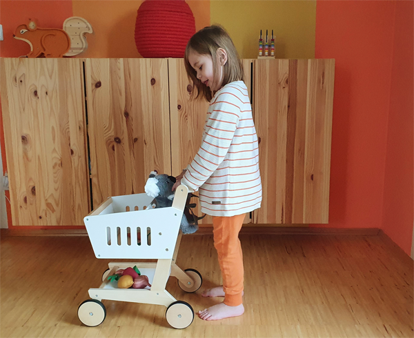 Kind mit Spiel-Einkaufswagen aus Holz