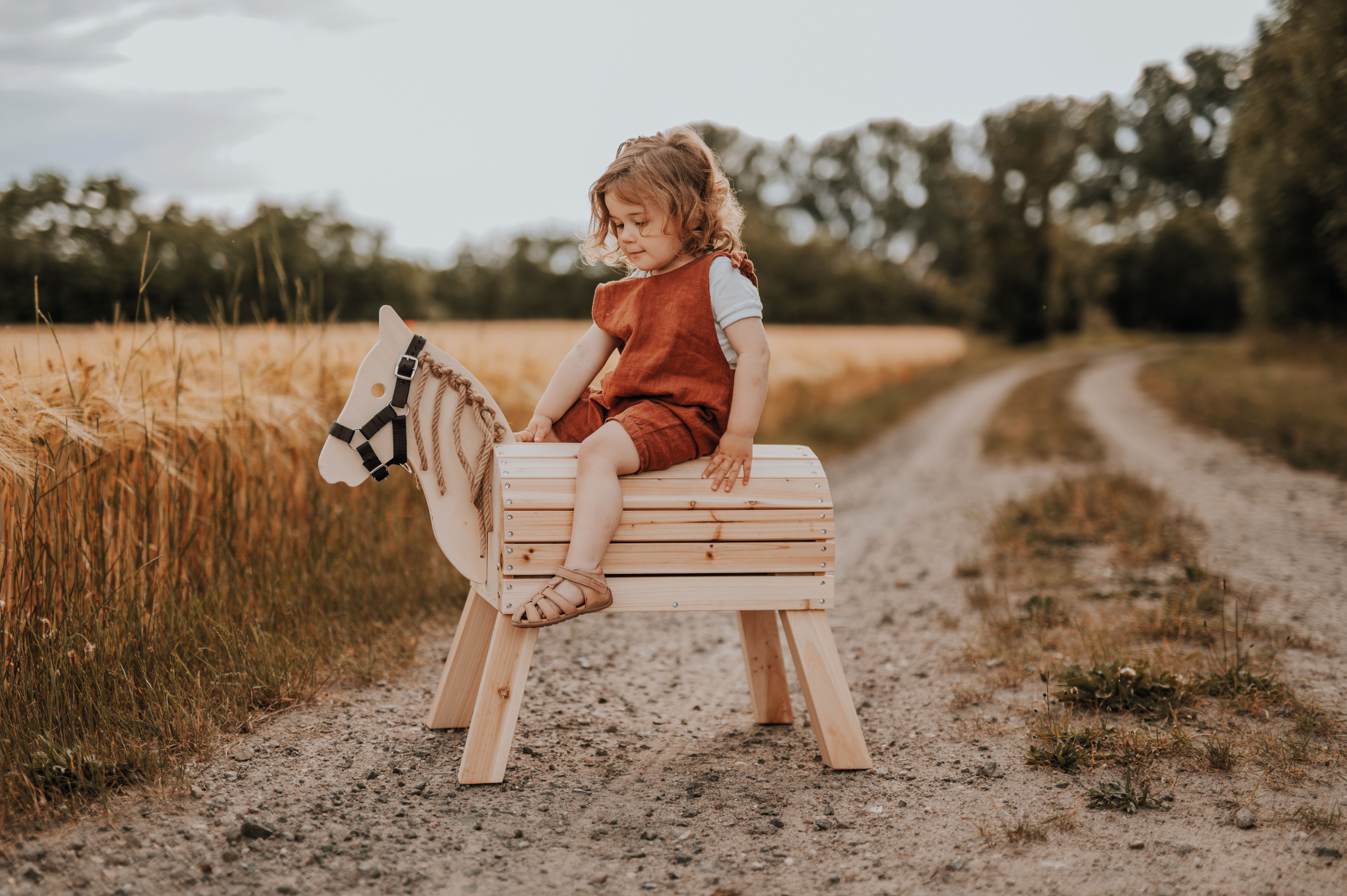 Mädchen reitet auf Feldweg auf einem Holzpferd