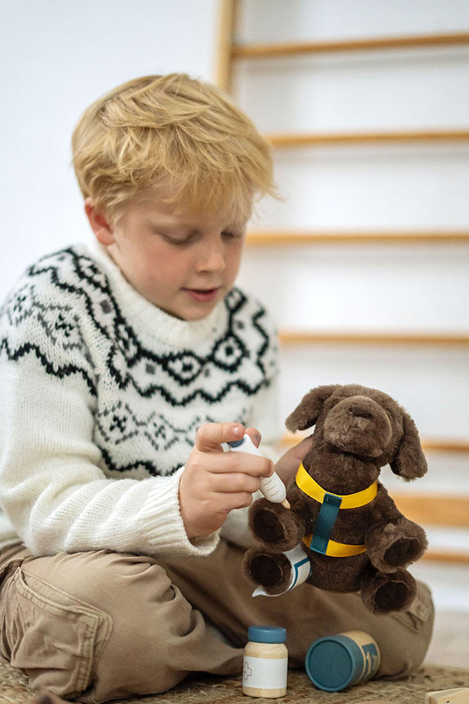 Kind spielt mit Plüschhund, Tasche und Pflegeset