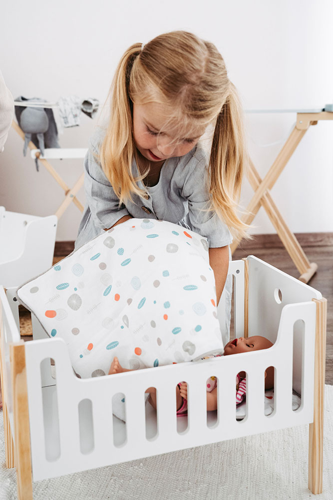 Kind legt Puppe ins Gitterbett